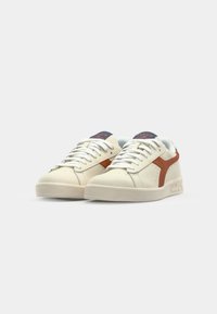 White leather sneakers featuring a brown accent stripe, round toe, and white laces. Textured rubber sole with a subtle logo detail on the tongue.