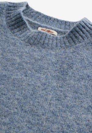 Light blue wool sweater with a ribbed crew neckline. Features soft, textured fabric and a label with "White Affinage" in red script.