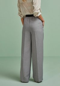 Szare spodnie o szerokich nogawkach wykonane z teksturowanej tkaniny, z fałdami z przodu i czarnym paskiem w talii, z widocznymi kieszeniami po bokach.