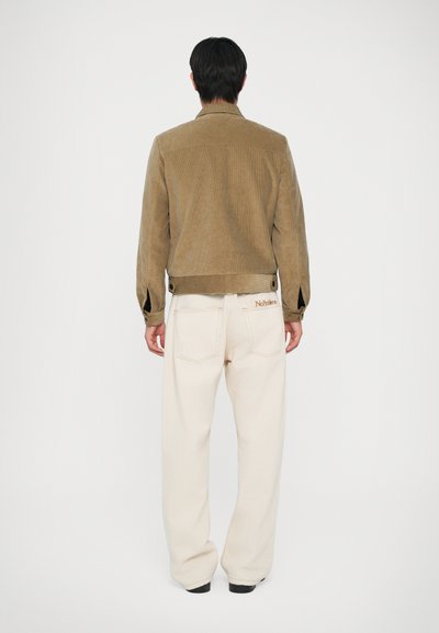 Brun kordfløjljakke med en cropped design, parret med cremefarvede vidde bukser med baglommer og lette stikninger.