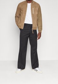 Tanarz suede bomber jacket z prążkowanymi mankietami, z zamkiem błyskawicznym, w połączeniu z czarnymi szerokimi spodniami i białymi sneakersami z czarnymi paskami.