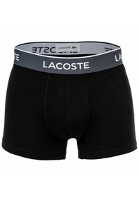 Boxer da uomo neri con elastico grigio, con testo bianco "Lacoste" e un piccolo logo verde di coccodrillo sull'etichetta interna.