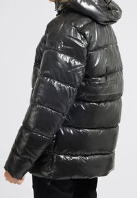 Černá péřová bunda s lesklým povrchem, s vodorovně prošívanými sekcemi a kapucí, která vykazuje hladkou texturu a elegantní design.