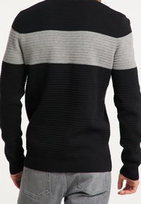 Schwarz-grau gestreifter Pullover aus strukturiertem Stoff mit gerippten Bündchen und Saum. Das Design enthält horizontale Rippenmuster.