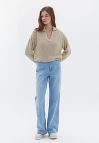 Beige stickad tröja med V-ringning och vida ärmar, kombinerad med hög midja ljusblå denimjeans och crème färgade plattformssneakers.