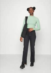 Top de manga longa em verde menta canelado com decote franzido, jeans flares pretos de cintura alta com fendas laterais e sapatos pretos.