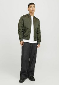 Olivengrøn bomberjakke, letvægtsstof, ribbede manchetter, parret med hvid T-shirt og vide mørk denim jeans, sorte chunky sko.