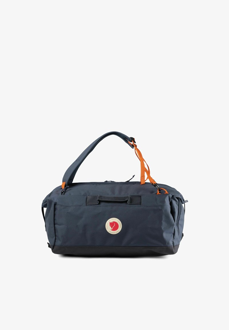 Sac polochon bleu marine avec base noire, tirettes de fermeture éclair orange, bandoulière réglable, patch logo avant et fermeture éclair supérieure.