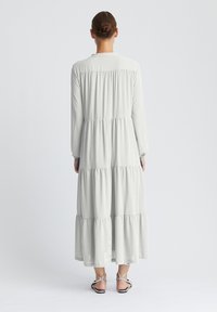 Robe longue gris clair en tissu doux, dotée d'un design à volants avec manches longues et poignets élastiques. Vue arrière montrant une silhouette lisse.