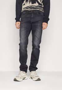 Mörkgrå jeans med slim fit, som har en subtil urtvättad textur. Bärs med en mönstrad tröja och ljusa sneakers.