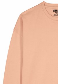 Sweat-shirt rose poussiéreux en coton, avec un col rond, des manches raglan et des détails de coutures visibles.