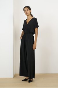 Svart jumpsuit i slätt material, med V-hals, korta ärmar, elastisk midja och vida ben. Matchad med svarta spetsiga skor.