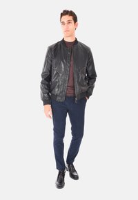 Giubbotto bomber in pelle nera con finitura liscia, chiusura con zip e polsini elasticizzati. Abbinato a pantaloni in corduroy blu navy e scarpe nere.