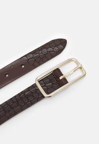 Curea din piele maro cu textură de crocodil embosată și cataramă din metal auriu. Are găuri ajustabile pe toată lungimea curelei pentru o potrivire ușoară.