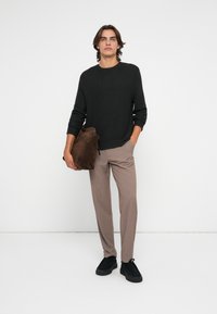 Zwarte gebreide trui, beige op maat gemaakte broek, gestructureerde bruin suède tas en zwarte sportieve schoenen. Eenvoudig, modern ontwerp met neutrale kleuren.
