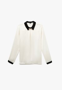 Blusa de manga larga en crema con cuello y puños negros, que presenta un pliegue frontal y acentos decorativos de perlas en el cuello. Textura suave.