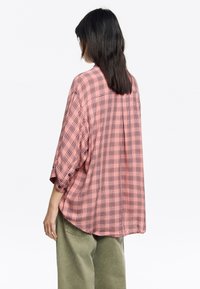 Camisa de cuadro rosa de gran tamaño con patrón de rejilla negra, puños abotonados y bajo curvado. Fabricada en tejido ligero con un corte holgado.