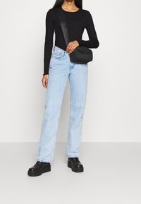 Schwarzes langärmeliges Oberteil, hellblaue gerade Jeans, schwarze Schultertasche und klobige schwarze Plateauschuhen. Glatte Texturen und einfaches Design.