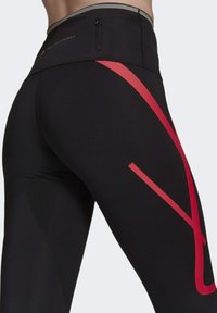 Czarne legginsy sportowe z wysokim stanem, z dużym czerwonym ukośnym paskiem i małą kieszonką na zamek z tyłu.