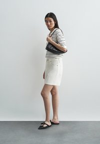 Fehér farmer szoknya fekete-fehér csíkos kötött felsővel, texturált fekete kézitáskával és fekete lapos cipővel párosítva.