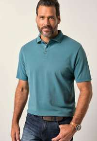 Turkusowa bawełniana koszulka polo z krótkim rękawem, z trzema guzikami i subtelną fakturą prążkowaną, zestawiona z ciemnoniebieskimi dżinsami i brązowym paskiem.