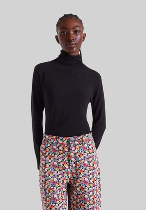 Top negro de cuello alto combinado con pantalones de estampado floral que presentan flores multicolores sobre un fondo claro. Textura suave en toda la prenda.