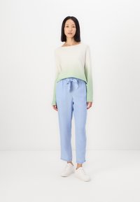 Sweater léger en dégradé de crème à vert, associé à un pantalon bleu clair avec un nœud à la taille et des poignets retroussés. Baskets blanches.