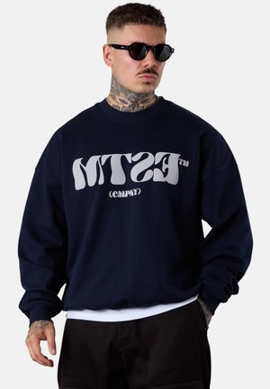 Navy blue sweatshirt made of cotton with a relaxed fit, featuring large white text "MTSTM" and "(CMPNY)" in a rounded, distorted font.