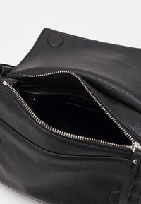 Sac en cuir noir avec fermeture éclair, surface texturée et design élégant, doté d'une poche à l'avant et d'une doublure intérieure.