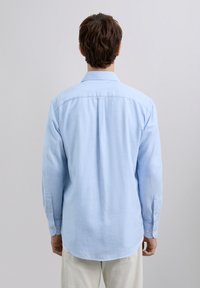 Chemise boutonnée bleu clair en coton, dotée d'un col, de manches longues et d'un ourlet arrondi avec une coupe décontractée. Design minimaliste.