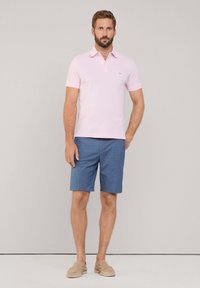 Lichtroze polo met korte mouwen en een klein logo, gecombineerd met marineblauwe shorts en beige instappers. Eenvoudig en casual ontwerp.