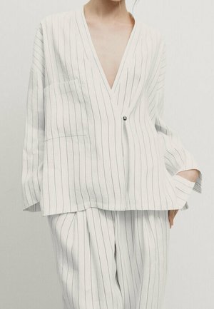 Woman wearing white pinstriped suit with oversized blazer fastened by single button and matching wide-leg trousers.