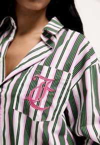 Csíkos ing, amely függőleges zöld, rózsaszín és fehér vonalakat tartalmaz, a mellzsebén pedig egy hímzett rózsaszín "F" betű található. Az anyag könnyűnek tűnik.