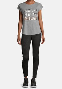 T-shirt grigio a maniche corte con testo metallico "FAI DI PIÙ DI CIÒ CHE AMI", abbinato a leggings neri e sneaker neri con dettagli dorati.