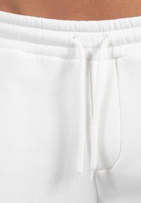 Sudadera blanca con cintura elástica, con cordón, textura suave y bolsillos laterales.