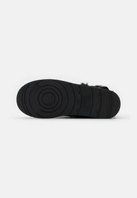 Calzature nere con suola in gomma testurizzata, caratterizzata da motivi circolari e una leggera elevazione. Accentuate da un materiale morbido simile alla pelliccia.