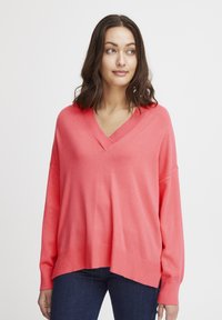 Pullover corallo con scollo a V realizzato in tessuto morbido, caratterizzato da maniche ampie e una vestibilità rilassata. L'orlo è leggermente più lungo sul retro.