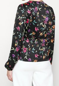 Svart blommig blus med långa ärmar, med färgglada blommor och blad, skrynklig midjedetalj och en slät satintextur.