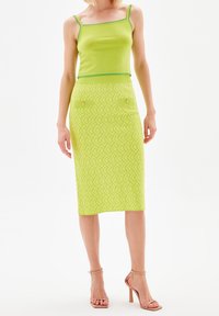 Grünes Crop-Top mit dünnen Trägern, kombiniert mit einem knielangen Bleistiftrock mit einem strukturierten geometrischen Muster und frontalen Taschen.