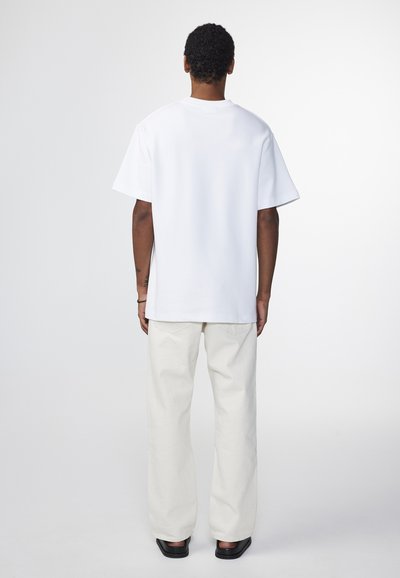 Weisses Baumwoll-T-Shirt mit lockerer Passform, kurzen Ärmeln und rundem Halsausschnitt, kombiniert mit hellen, weiten Hosen und schwarzen Schuhen.
