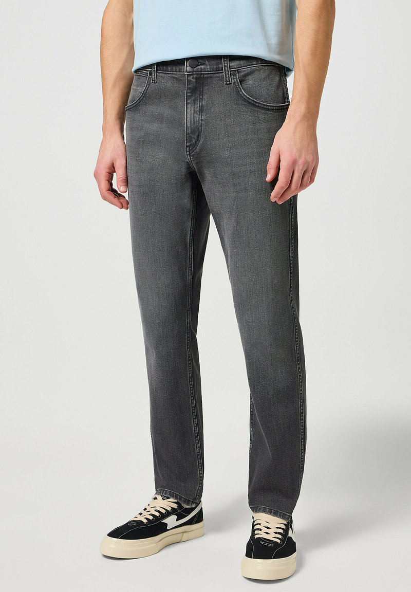 Jeans de denim gris con pierna recta, diseño de cinco bolsillos, costuras visibles y un ligero desvanecimiento. Combinados con zapatillas en negro y crema.