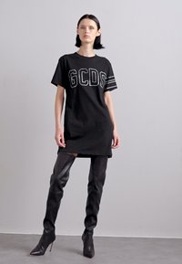 Μαύρο κοντομάνικο φόρεμα φανέλα με λευκό λογότυπο "GCDS" και ριγέ λεπτομέρειες, συνδυασμένο με μαύρες μπότες μέχρι το μηρό. Λείο υλικό.