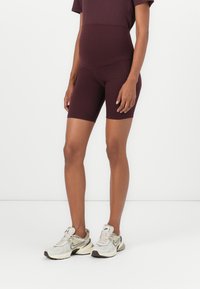 Calções atléticos bordeaux com cintura alta e design ajustado, combinados com sapatilhas Nike em bege e cinza com tecido texturizado e atacadores.