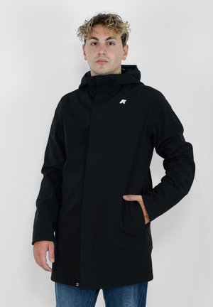 Giacca nera impermeabile con cappuccio fisso, zip frontale e tasche laterali; presenta un logo sul petto e una superficie liscia e opaca.