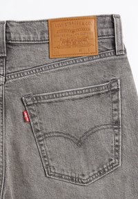 Poche arrière d'un jean en denim gris avec une étiquette rouge Levi's et un patch en cuir marron de la marque Levi Strauss & Co. au-dessus de la poche.