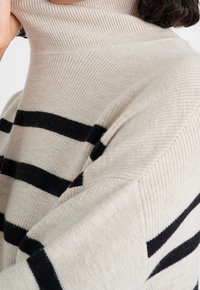 Krémový rolákový svetr s černými horizontálními pruhy, pletená textura a volný střih, s vysokým límcem a spadlými ramenními švy.