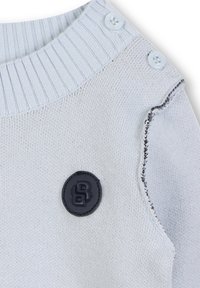 Maglione lavorato a maglia azzurro chiaro con scollo a coste, due bottoni bianchi sulla spalla e un logo circolare nero sul davanti.