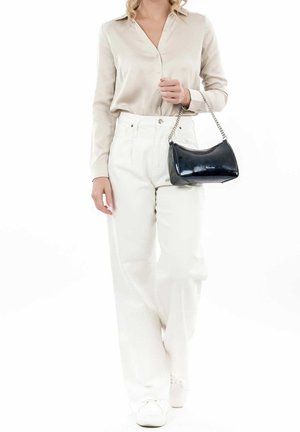 Femme portant un chemisier en satin beige et un pantalon blanc à jambes larges, tenant un petit sac à main noir avec une lanière chaîne argentée.