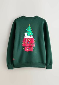 Zöld pulóver, amelyen Snoopy grafikája látható egy piros kutyaháztetőn, színes karácsonyi égőkkel díszítve és egy feldíszített fával.