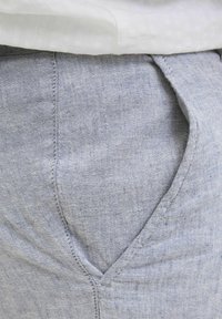 Tissu bleu clair avec une texture lisse, présentant une poche latérale, des coutures bordées et un léger brillant. Le tissu semble tissé et doux.